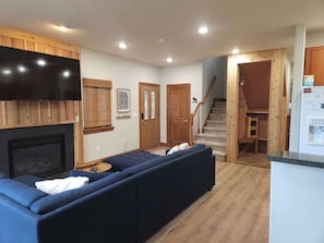 A living room with a fireplace, a large flat-screen TV, a wooden ceiling, and a staircase leading to another level. - Family Hot Tub, Mountainscape Chalet! Paradise! (Breckenridge)