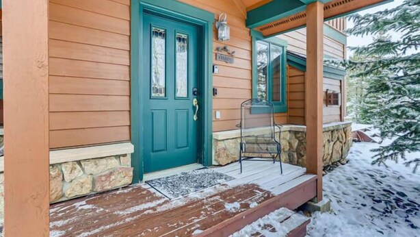 A wooden cabin with a green door, stone foundation, and a porch with a chair. - Family Hot Tub, Mountainscape Chalet! Paradise! (Breckenridge)