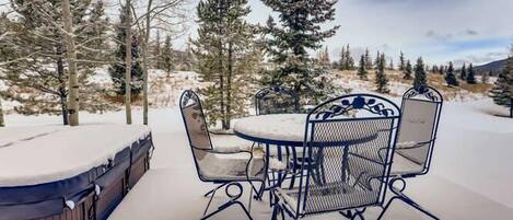 Un patio cubierto de nieve con una mesa redonda y sillas, rodeado de árboles.