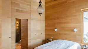 Ein modernes Schlafzimmer mit einem großen Bett, Holzwänden, einer Pendelleuchte und Blick durch ein Fenster.