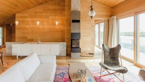 Ein modernes Interieur mit Holzbalkendecke, einem weißen Sofa, einem Kamin und großen Fenstern.