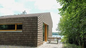 Ein modernes Haus mit Satteldach, einem großen Fenster und einer Terrasse mit Tisch und Stühlen.