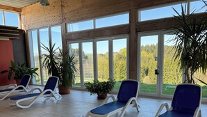Un espacio interior iluminado por el sol, con ventanas amplias, sillones de descanso y plantas en macetas.