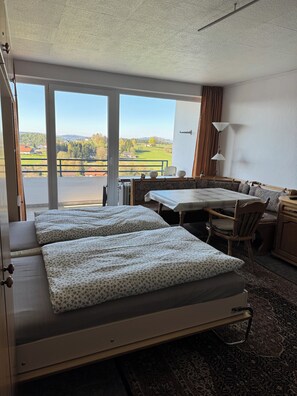 A hotel room with a bed, a desk, a chair, a table, and a view of the countryside.