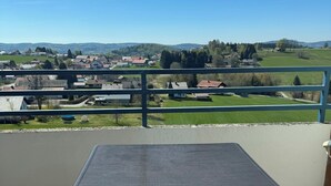 Un balcón con mesa y sillas, con vistas a un paisaje rural con casas y vegetación.