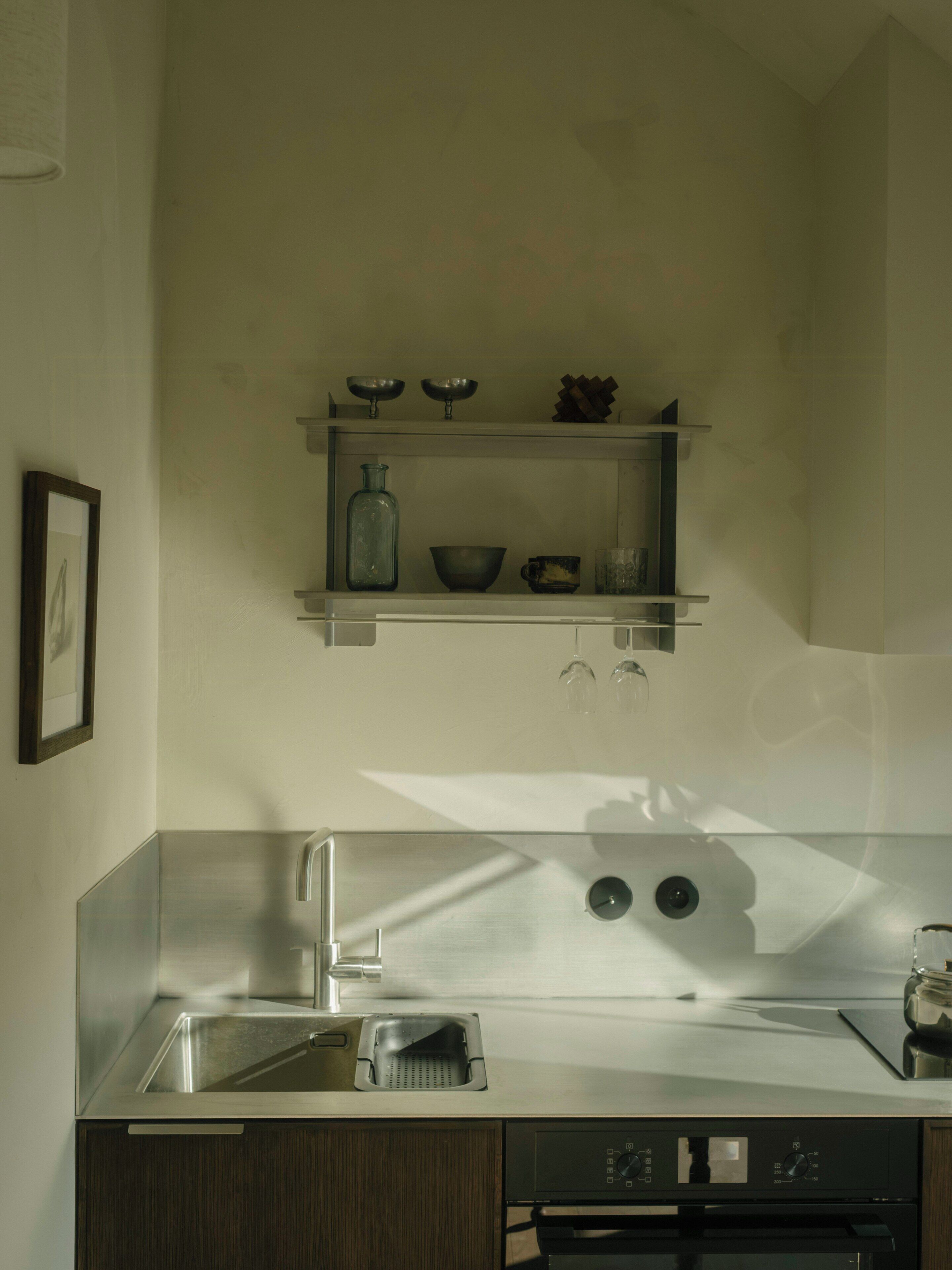 Una cocina moderna con un fregadero de acero inoxidable, lavavajillas y horno empotrado. Hay una repisa sobre el fregadero con distintos utensilios de cocina.