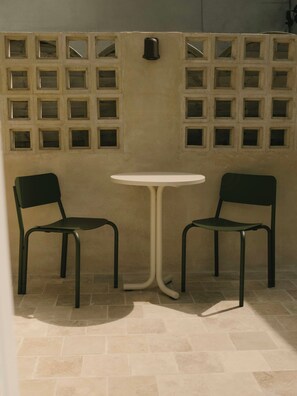 A room with a tiled floor, a white round table, two black chairs, and a wall with multiple square windows. - Sea view apartment in Saint Cado Brittany (Belz)