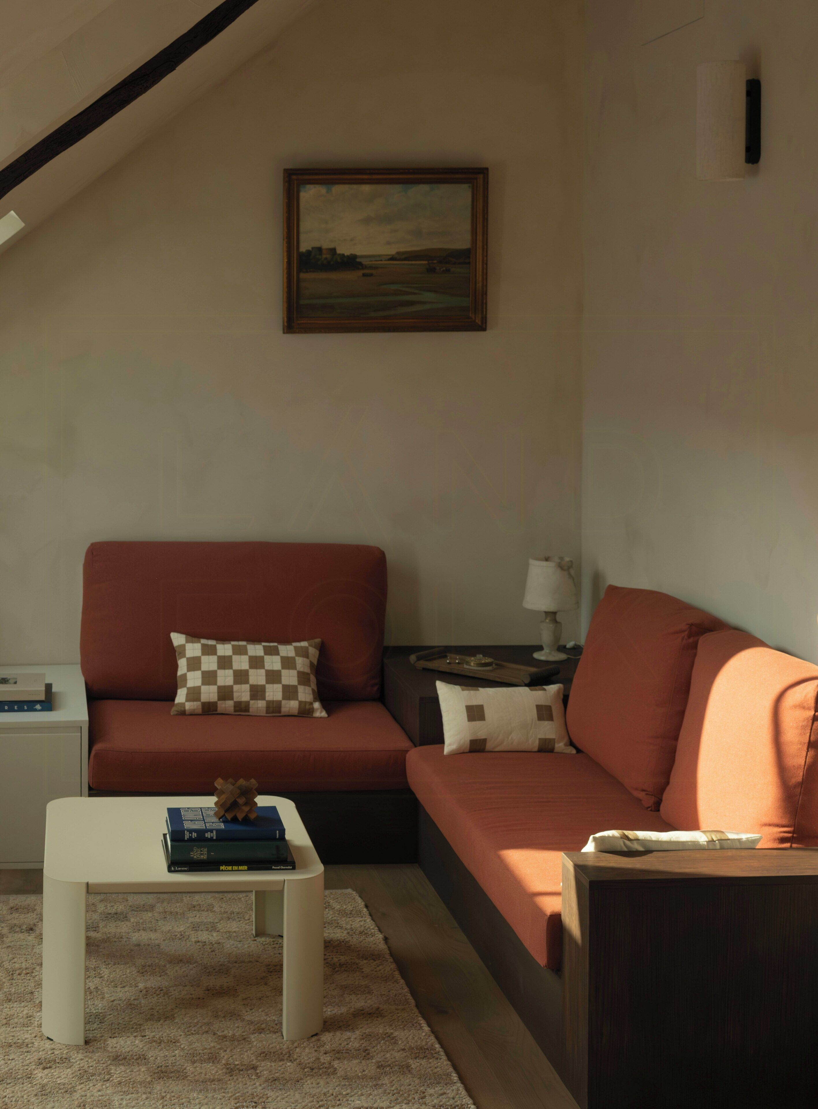 A living room with a sofa, a coffee table, a painting on the wall, and a lamp on a side table.
