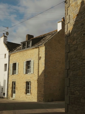 A stone building with a sloped roof, multiple windows with shutters, and a visible satellite dish. - Sea view apartment in Saint Cado Brittany (Belz)