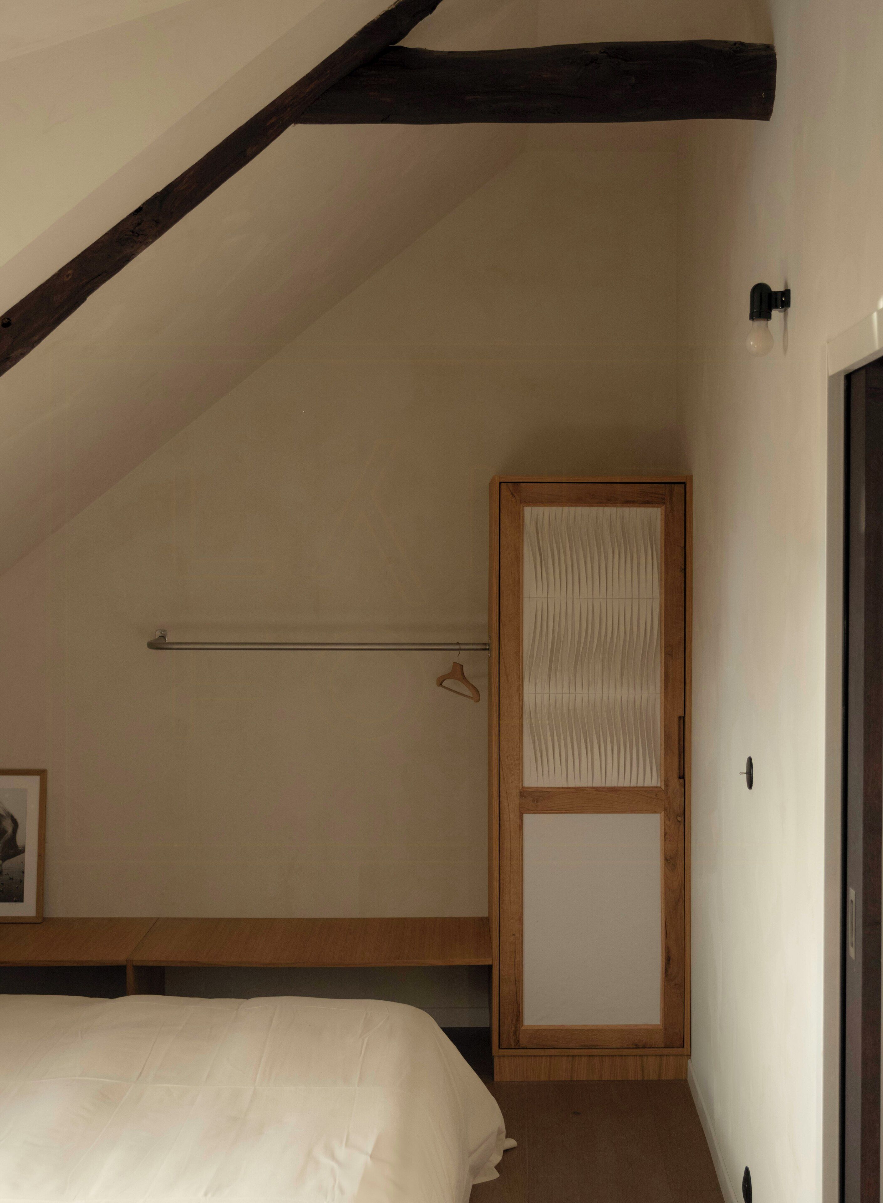 Un dormitorio con techo inclinado, una cama, un armario de madera y una lámpara colgante.