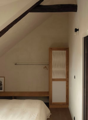 A bedroom with a sloped ceiling, a bed, a wooden wardrobe, and a hanging light fixture. - Sea view apartment in Saint Cado Brittany (Belz)