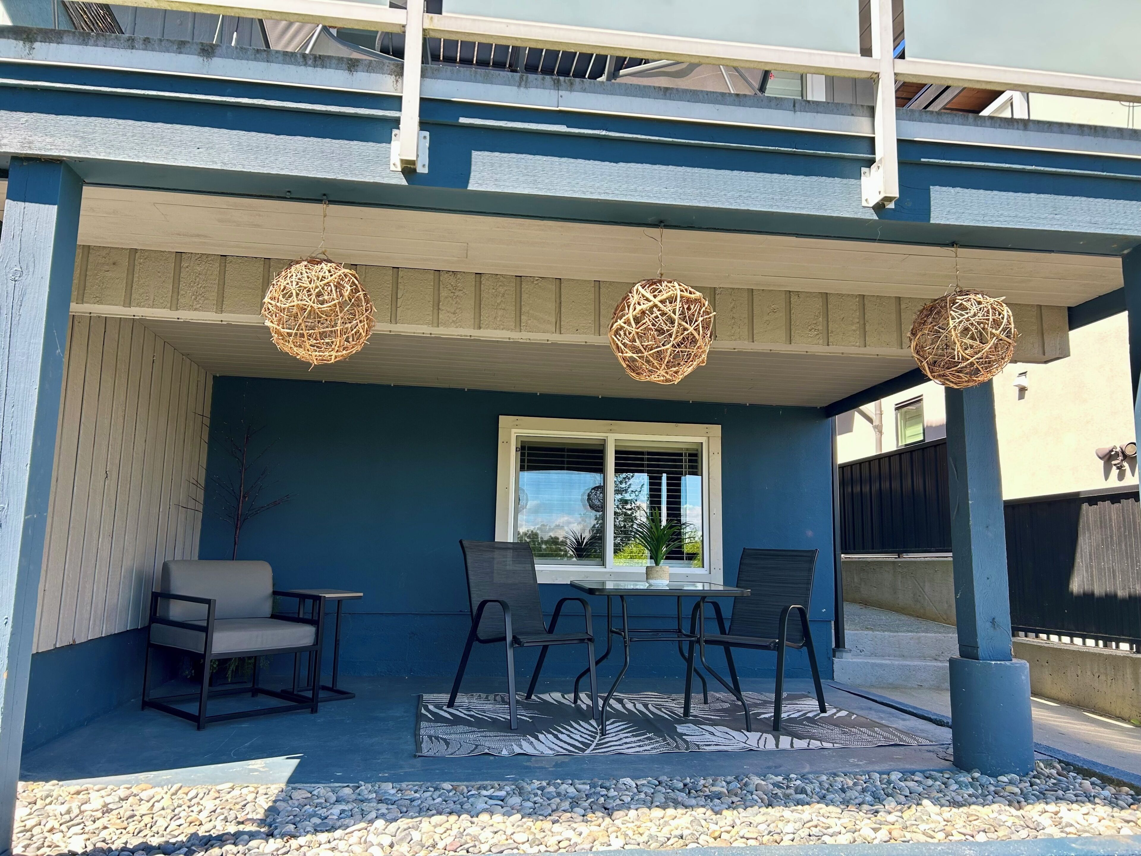Une terrasse couverte avec des sièges d’extérieur, une fenêtre et des sphères décoratives en osier.