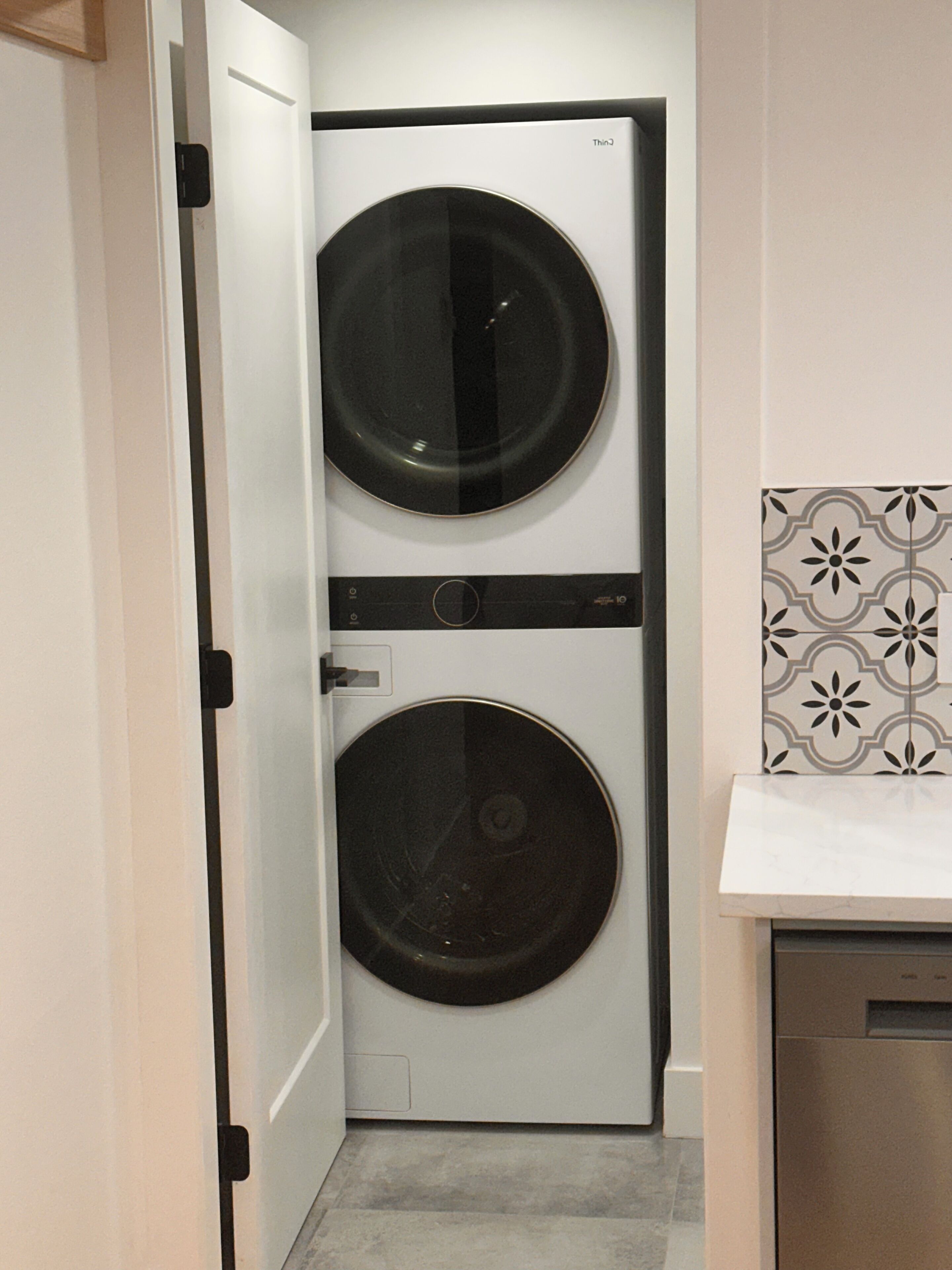A compact laundry room with two stacked washing machines, a door, and a patterned tile backsplash.