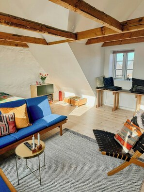 A loft-style living room with exposed wooden beams, a blue sofa, a patterned armchair, and a small table with candles. - Townhouse from 1862 with sunsets in Thorøhuse (Assens)