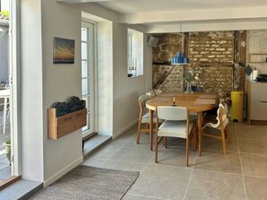 A dining area with a wooden table, chairs, a vase with flowers, a brick wall, and a window with a view. - Townhouse from 1862 with sunsets in Thorøhuse (Assens)