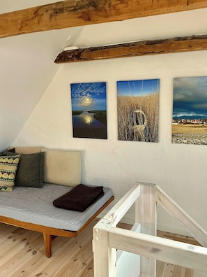 A loft-style room with a sloped ceiling, a wooden beam, a bed with striped bedding, and three framed landscape paintings. - Townhouse from 1862 with sunsets in Thorøhuse (Assens)