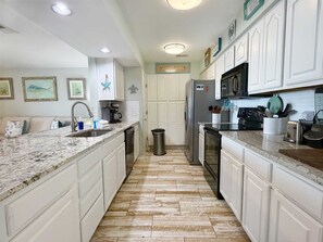 A kitchen with white cabinetry, a granite countertop, a stainless steel refrigerator, and a microwave. - Bayview 66 Townhome | Orange Beach Condo with Deeded Boat Slip + Boat Launch | Wolf Bay (Orange Beach)