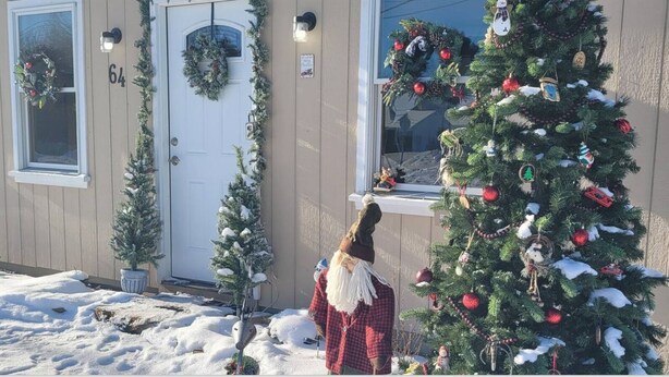Ein Wohngebäude mit verschneitem Balkon, einem Weihnachtsbaum und einer Gartenzwerg-Figur.