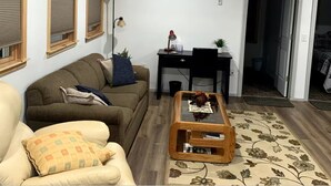 Ein Wohnzimmer mit einer Couch, einem Sessel, einem Couchtisch und einem Schreibtisch mit Stuhl.