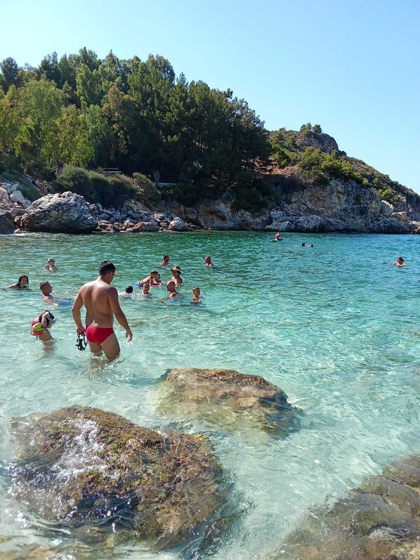 A clear coastal water body with people swimming and a rocky shoreline.