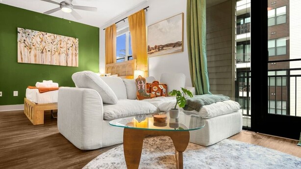 Uma sala de estar moderna com uma mesa de centro de vidro, um sofá, uma pequena mesa de madeira e uma parede verde.