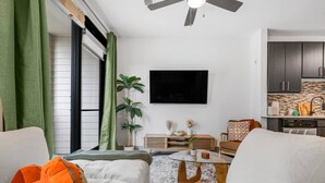 Uma sala de estar moderna com sofá, mesa de centro, televisão e área de cozinha com armários e bancada.