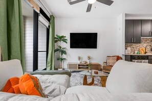 A modern living room with a sofa, a coffee table, a TV, and a kitchen area with cabinets and a countertop. - 5 mins to Broadway. Downtown. Midtown. Pool. Gym (Nashville)