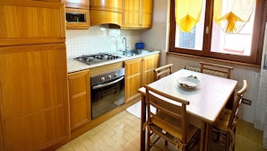 Een keuken met houten kastjes, een gasfornuis, een oven, een spoelbak en een eettafel met stoelen.