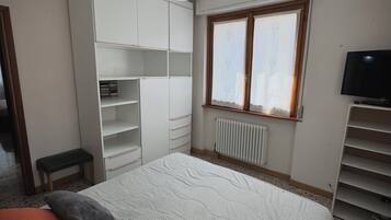 A bedroom with a bed, a wardrobe, a radiator, a window with curtains, and a television.