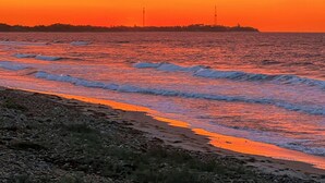 Una playa con olas, un atardecer y una costa lejana.