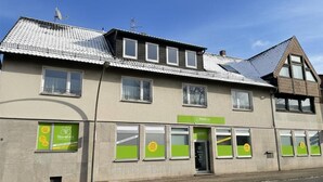 Een gebouw met pannendak, meerdere ramen en een etalage met groene borden.
