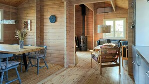 Interno di una baita in legno con zona pranzo, divano, camino e angolo cottura.