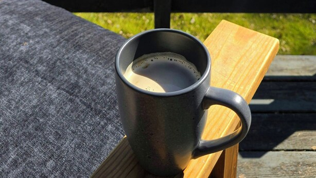 Una tazza di metallo su una panchina di legno, con vista su un prato e uno specchio d'acqua sullo sfondo.
