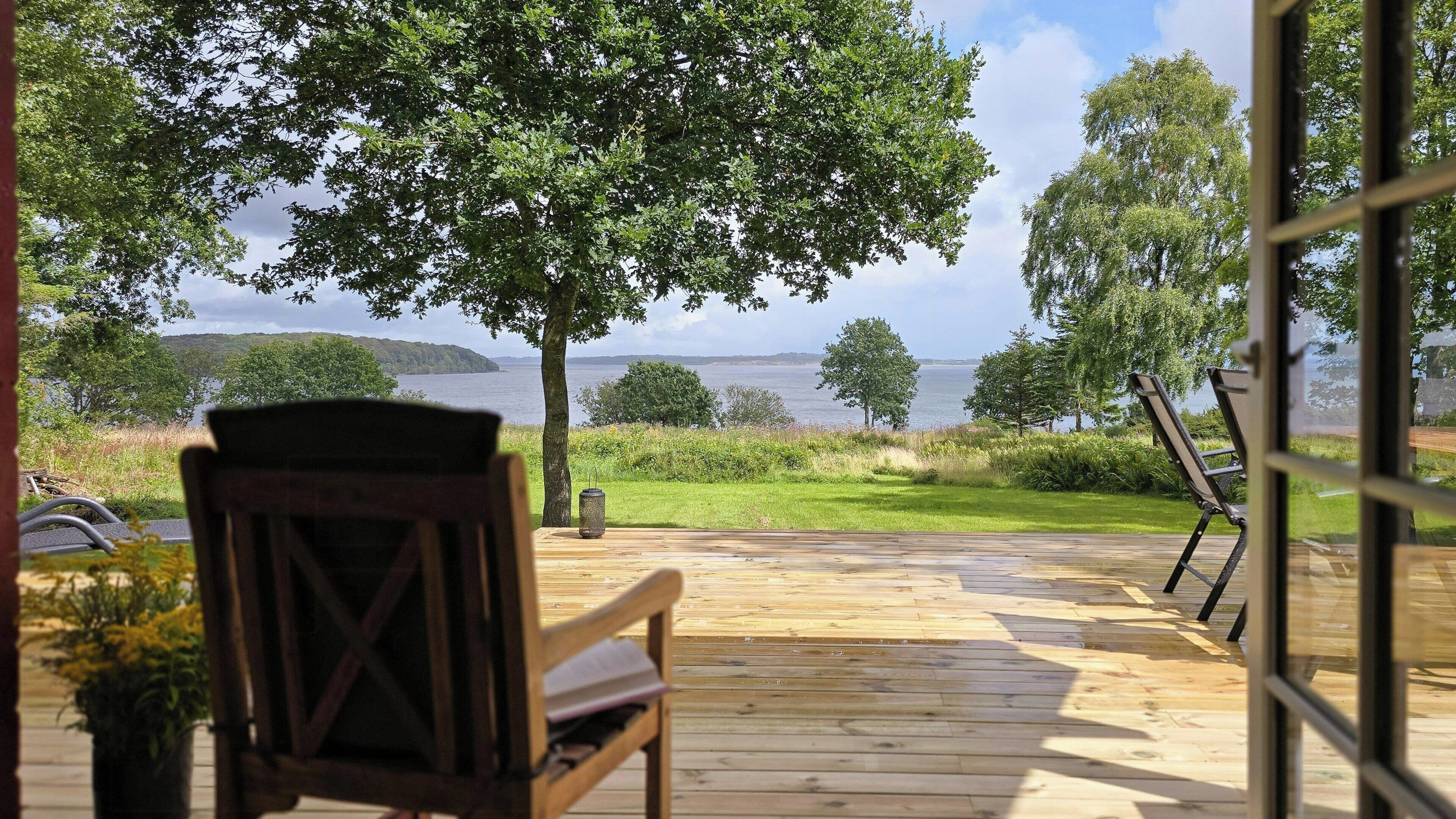 A wooden deck with a chair, a view of a lake, and trees in the background.