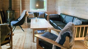 Un accogliente interno di una baita con pavimento in legno, un divano, una poltrona, un tavolo e un camino.