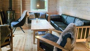 A cozy cabin interior with a wooden floor, a sofa, a chair, a table, and a fireplace. - Red timber house with fjord view (Roslev)