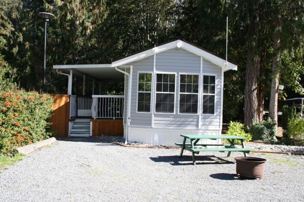 A small, single-story cabin with a porch, a picnic table, and a trash bin.