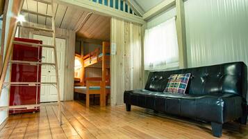 Una habitación con una cama litera, un sofá de cuero negro, una escalera de madera y un armario rojo.