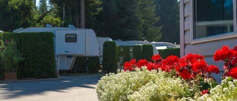Ein Wohngebiet mit einem weißen Wohnmobil auf der Auffahrt, umgeben von ordentlich geschnittenen Hecken und blühenden Pflanzen.