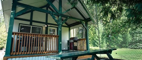 A covered outdoor area with a picnic table, a grill, and a fenced garden.