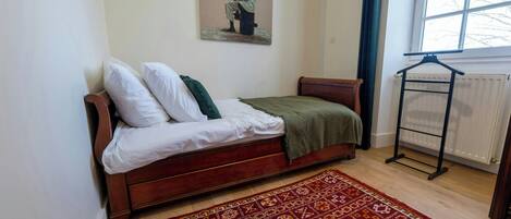 Un dormitorio con una cama de madera, un tapete estampado, un radiador y una ventana con vista a árboles.