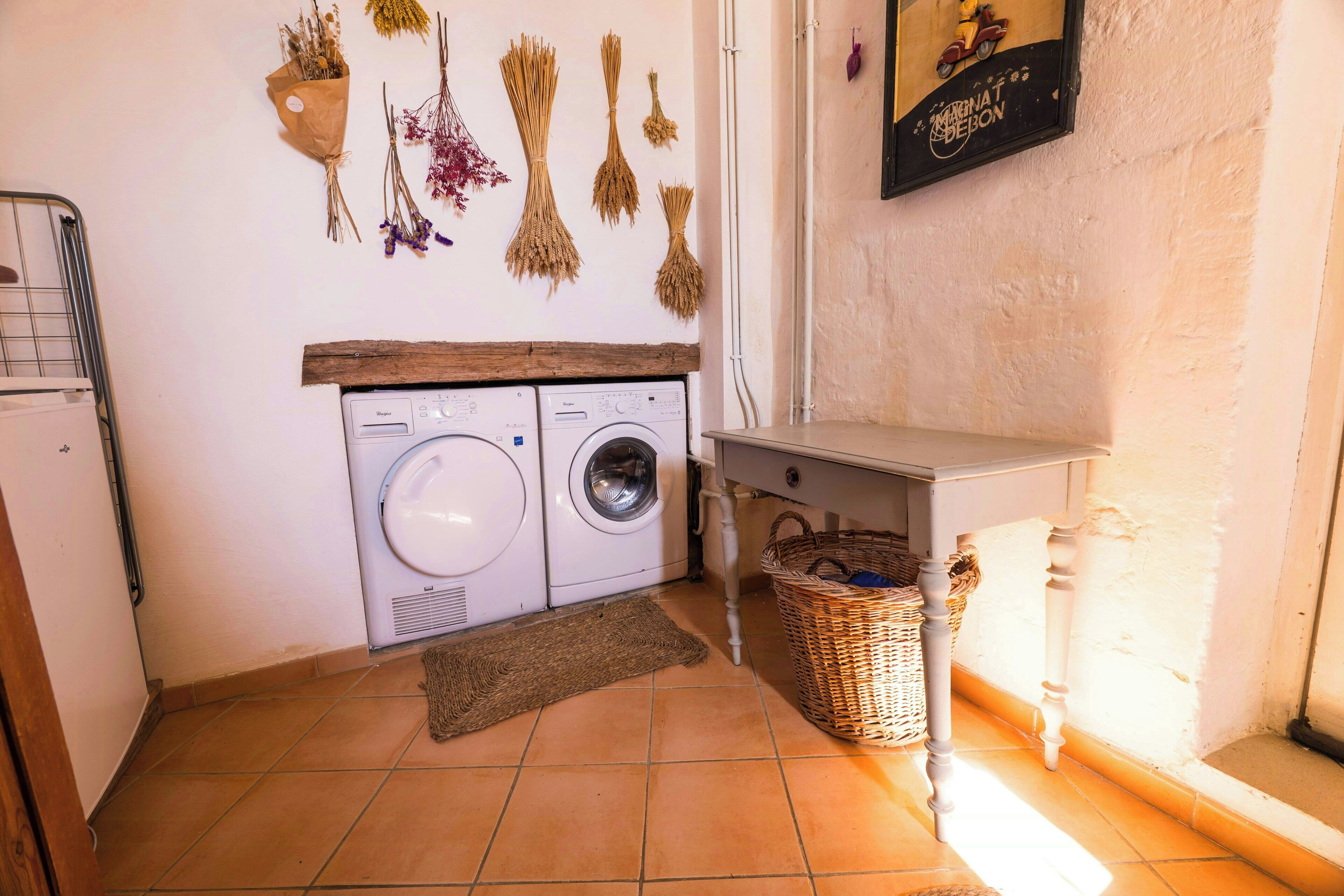 A laundry area with a washing machine, a drying rack, a wicker basket, and a framed picture on the wall.