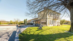 Un grand bâtiment à deux étages doté d’un balcon, entouré d’une pelouse bien entretenue et d’un chemin de gravier.