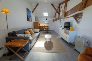 A living room with a sofa, coffee table, and a TV. There's a kitchen in the background with a dining table and chairs.