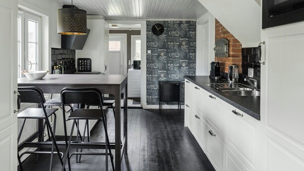 A modern kitchen with a black and white color scheme, a large island, and a coffee-themed wall. - Swedish cottage by forest and lake in Småland (Traryd)