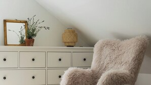 A room with a fluffy chair, a small stool, a white dresser, a mirror, a potted plant, and a woven basket. - Swedish cottage by forest and lake in Småland (Traryd)