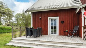 A red wooden building with a white door, a small deck with outdoor furniture, and a metal railing. - Swedish cottage by forest and lake in Småland (Traryd)