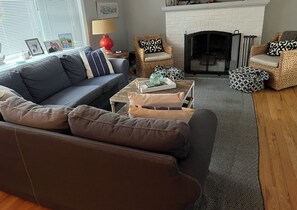 Ein Wohnzimmer mit grauem Sofa, Couchtisch, Kamin und Korbstühlen.