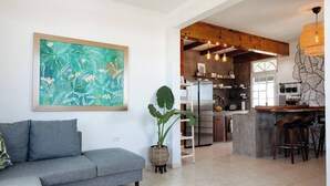 A modern kitchen with a bar area, a grey sofa, and a large abstract painting on the wall. - Oceanfront Rustic Family Home Fully Equipped for 8 (Camuy)