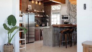 A kitchen with a wooden ceiling, hanging light bulbs, a refrigerator, and a bar area with stools. - Oceanfront Rustic Family Home Fully Equipped for 8 (Camuy)